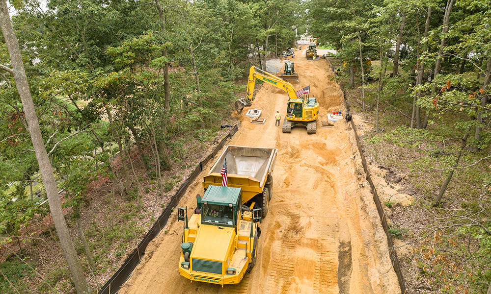 An excavator and dump truck drive through a forest for an Earle project.